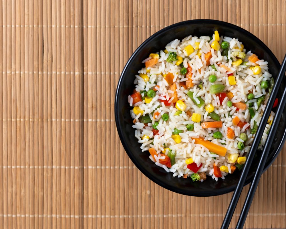 White fried rice with vegetables on wooden table. Top view. Copy space